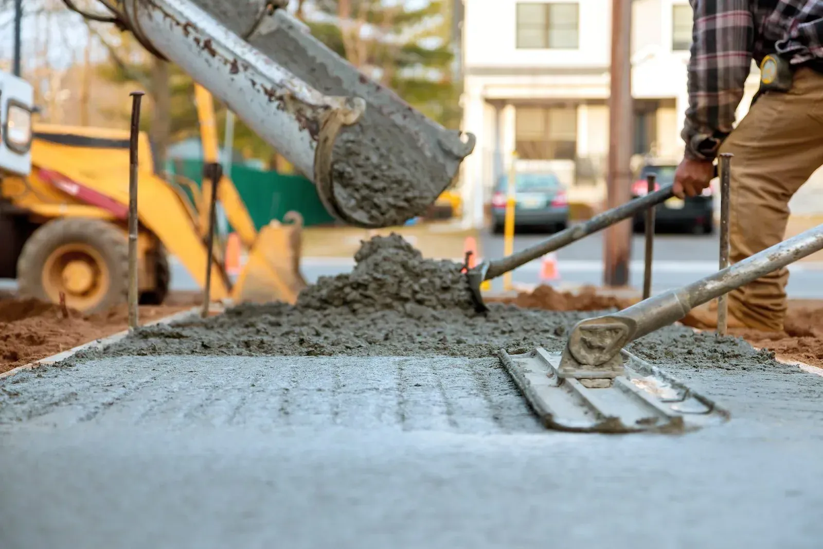 A chute pouring fresh concrete as a worker screeds the slab with a bull float