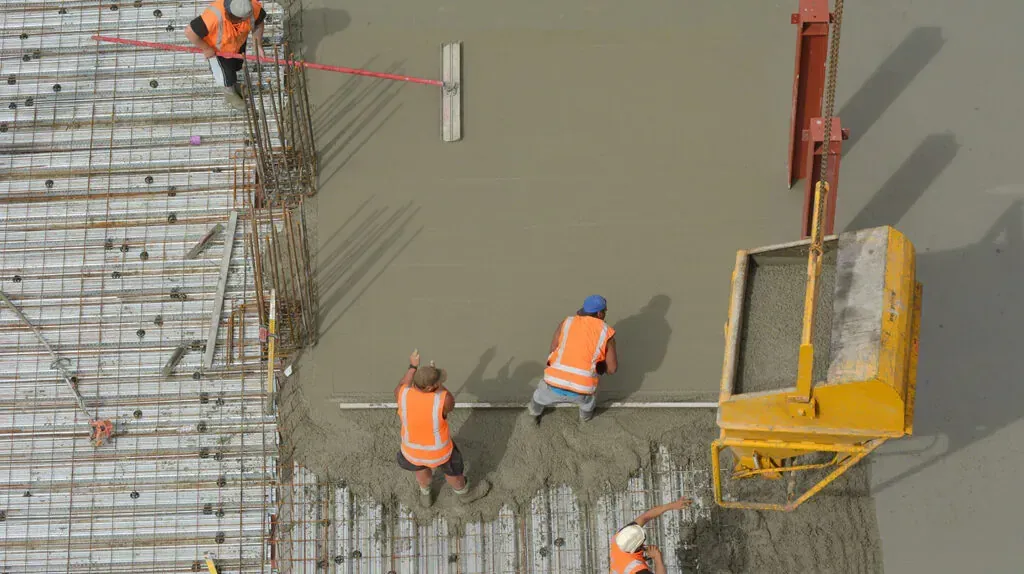 An aerial view of a crew screeding a large concrete slab pour fed by a crane hopper