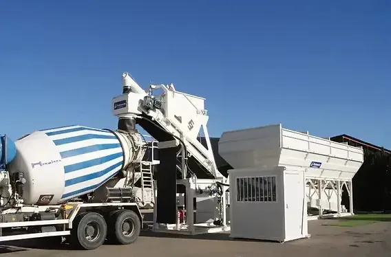 A ready-mix mixer truck with a striped drum loading at a concrete batch plant