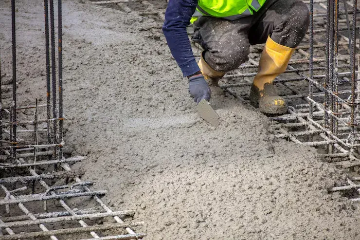 A worker kneeling to trowel fresh concrete among reinforcing bar