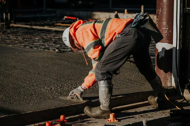A worker in a hi-vis shirt hand-troweling the edge of a fresh concrete slab at dusk