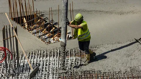 A worker in a hi-vis vest guiding a concrete pump pipe over rebar and formwork on a foundation pour — concrete contractor insurance