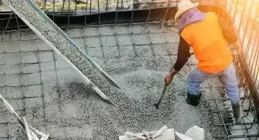 A worker shoveling and spreading fresh concrete across a rebar-reinforced deck — concrete contractor insurance