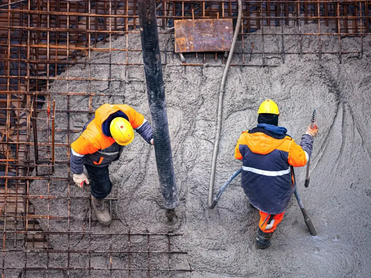 Two workers placing concrete through a pump hose into a deep rebar-reinforced foundation wall — concrete contractor insurance in Arkansas