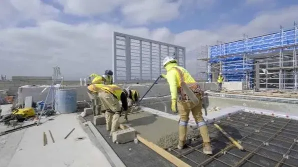 A crew screeding and placing fresh concrete on an elevated deck beside scaffolding — concrete contractor insurance in Washington