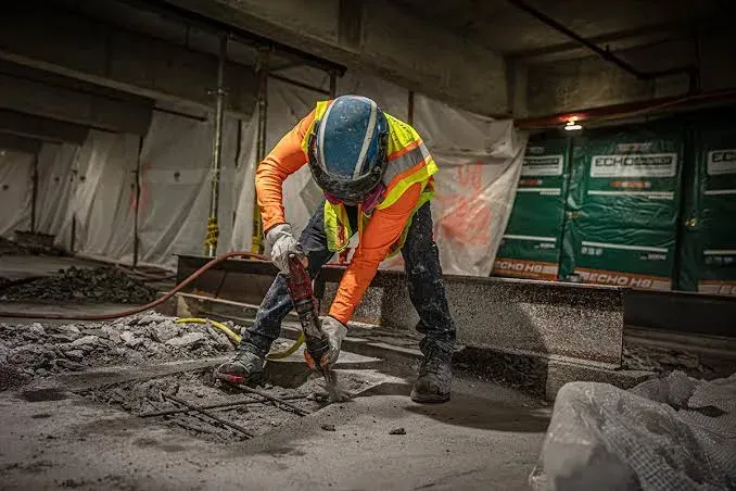 A worker breaking up a concrete slab with a demolition hammer in a parking structure — concrete business insurance