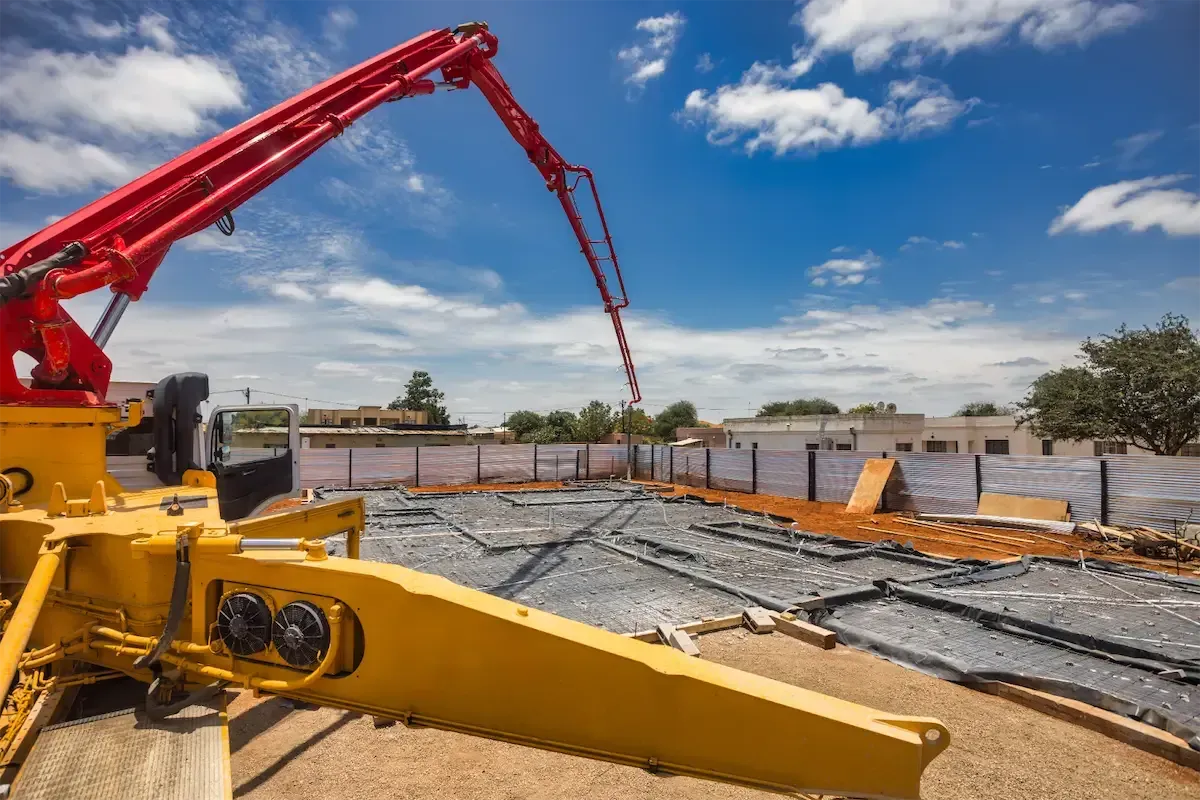 A red articulated boom pump reaching over a foundation pad laid with rebar and a vapor barrier — concrete pumping insurance in Ohio