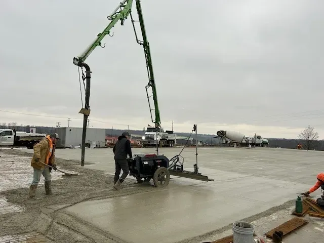 A boom pump placing concrete into a ride-behind laser screed as mixer trucks wait — concrete pumping insurance in Florida