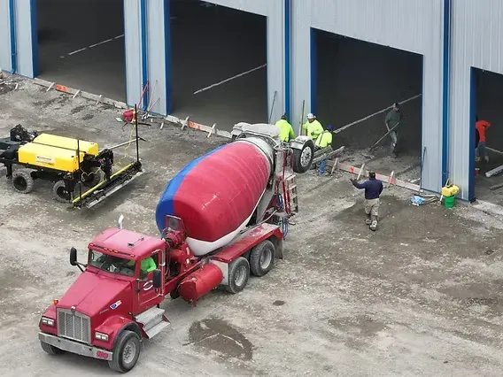 A ready-mix mixer discharging concrete into a warehouse slab pour beside a laser screed — ready-mix concrete insurance in Utah